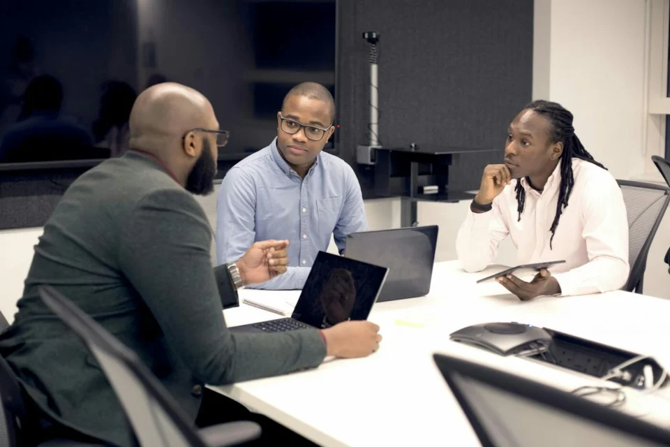 Three colleagues working on laptops around a table in a modern office