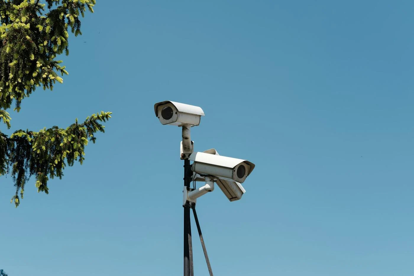Two CCTV cameras mounted on a pole against a clear blue sky